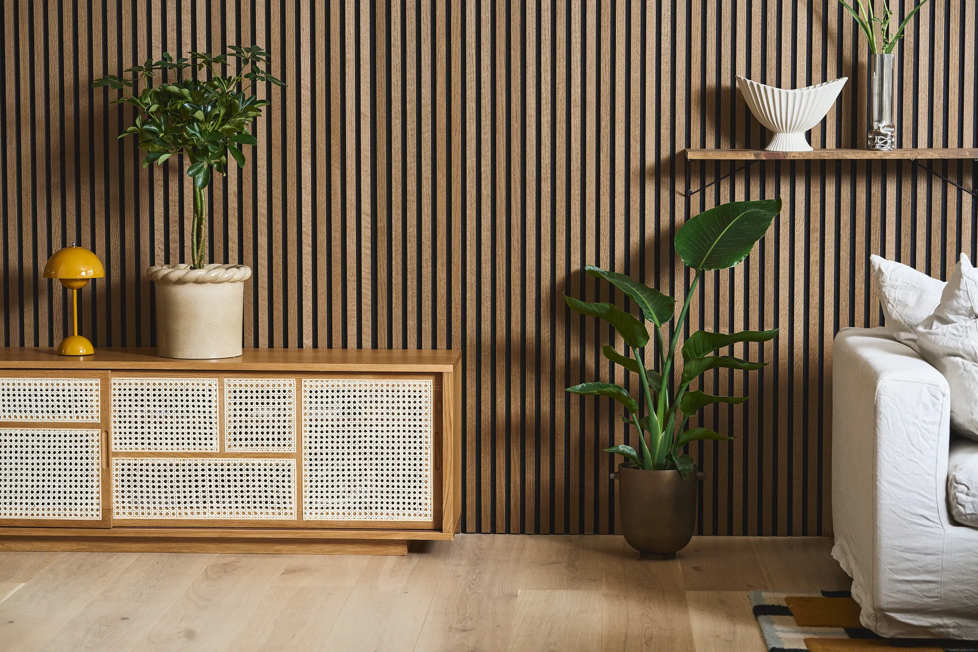 Moderni olohuone, jossa rimaseinä, rottinkikaappi, keltainen lamppu, huonekasveja ja valkoinen sohva.