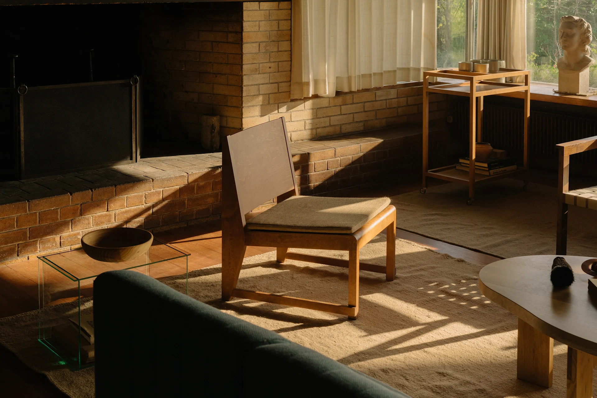Aurinkoinen olohuone, jossa on tiilitakka, puinen tuoli ja vihreä sohva, ikkunan vieressä rintakuva.