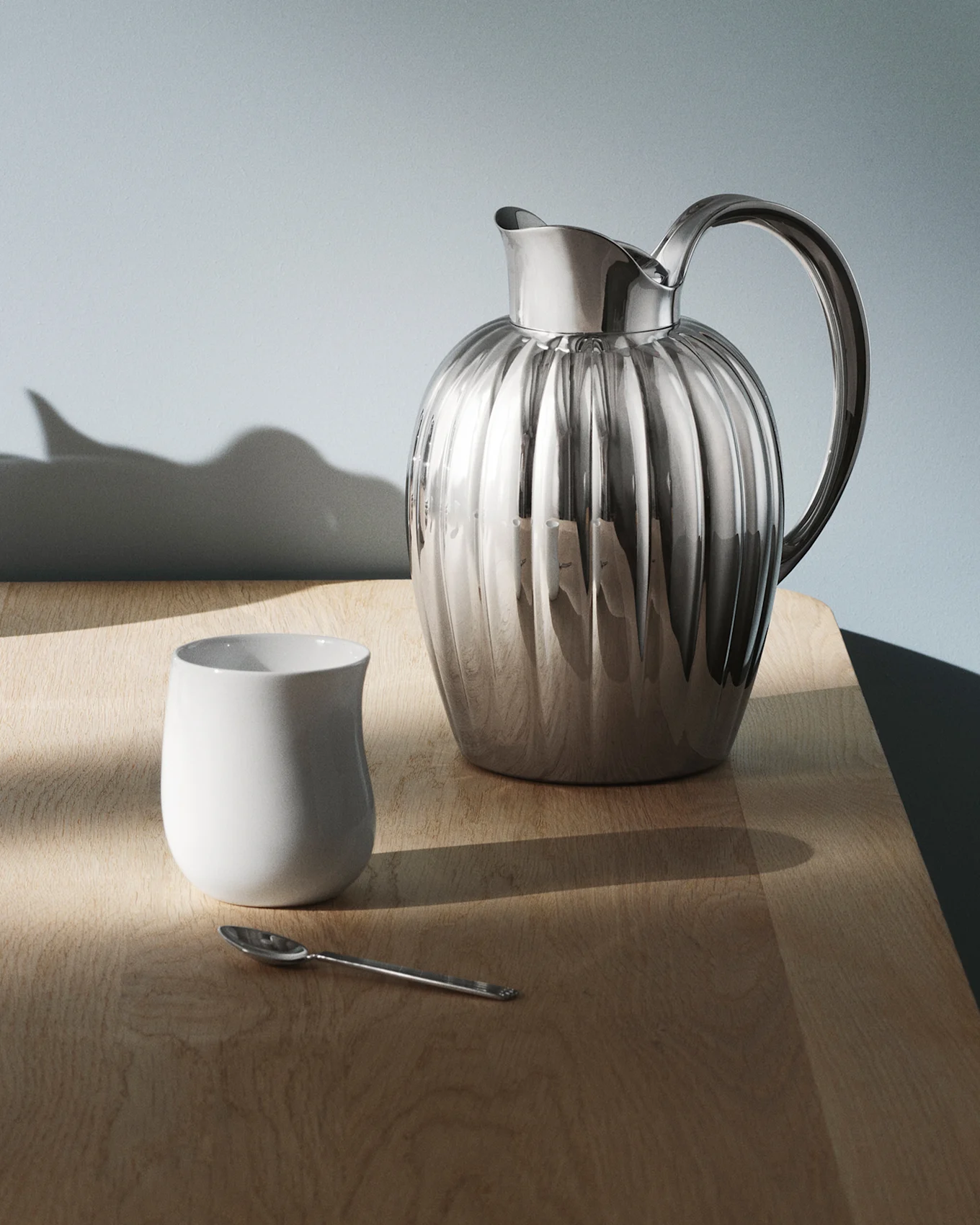 Kiiltävä, uurrettu hopeinen kannu ja kahva tummalla, heijastavalla pöydällä, valokuvioita pinnalla.