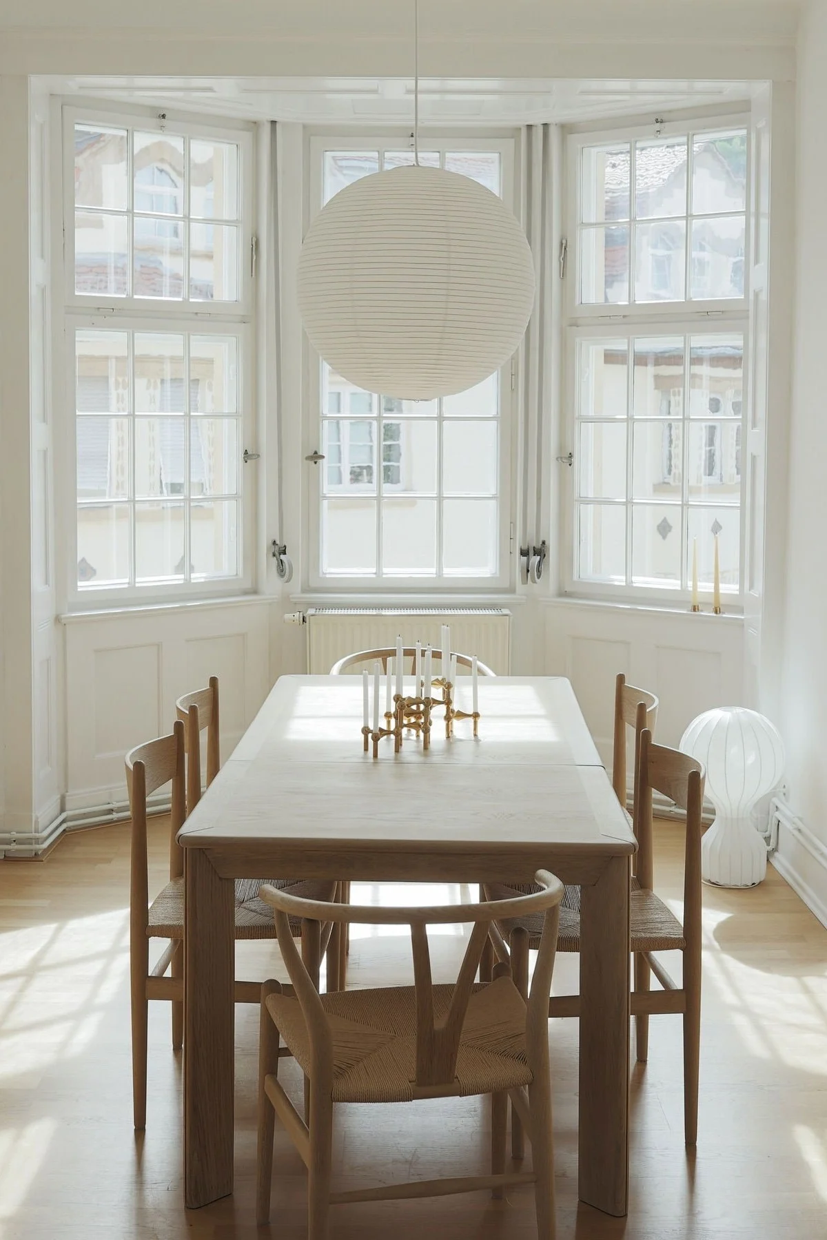 Lagom-sisustus on minimalistinen. Tässä näet @b.wohnbarin ruokasalin, jossa on suuri ruokapöytä, tuolit, korkeat ikkunat ja HAY:n Paper rice -riippuvalaisin.