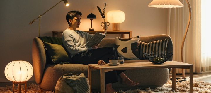 Oikean hehkulampun valinta on tärkeää kodin tunnelman kannalta - mies istuu sohvalla eri valonlähteiden ympäröimänä ja lukee kirjaa. 