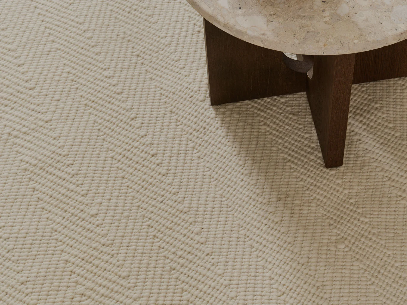 Lähikuva kermanvärisestä kuvioidusta matosta, jossa on kalanruotokuvio, pöydän vieressä, jossa on kivitaso.