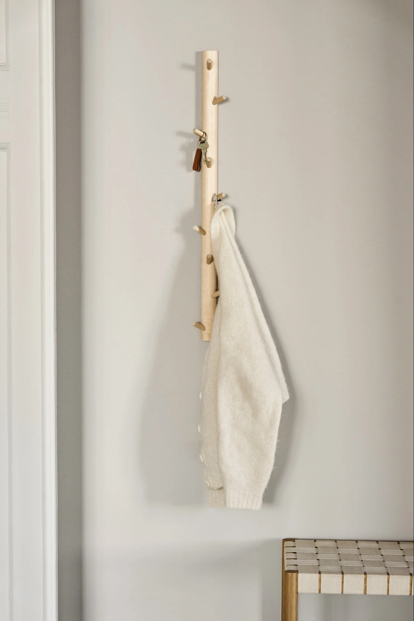 Vaalea puinen koukkulista pitää avaimia ja kermanvalkoista villapaitaa, jonka alla on punottu penkki.