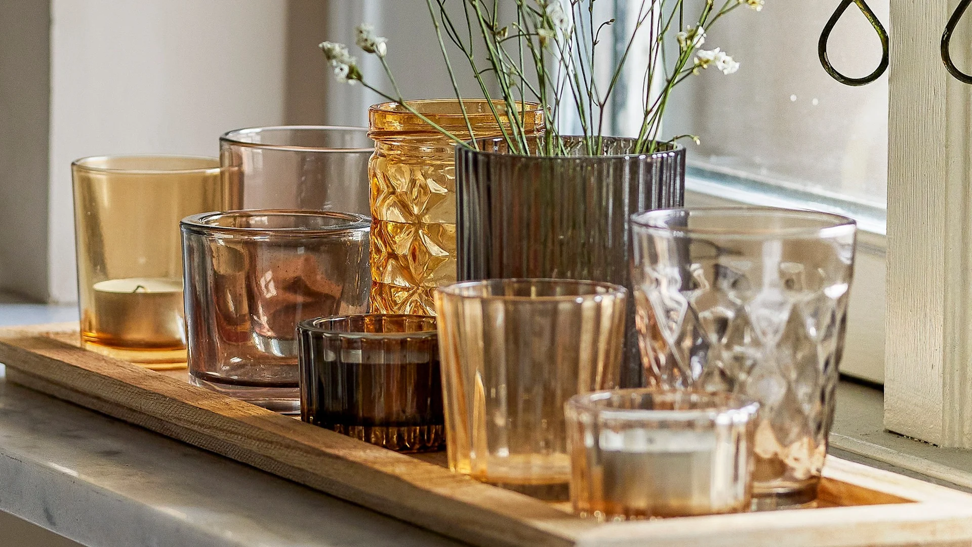 Täydellinen boho-sisustus: Bloomingvillen Sanga-tarjotin, jossa on eri kelta- ja ruskeasävyisiä teekynttilänjalkoja, seisoo ikkunalaudalla.