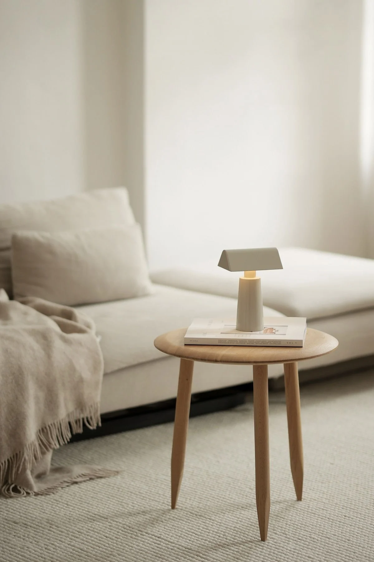 Lagom-tyylinen sisustus on tunnettu hillityistä väreistä. Tässä näet @b.wohnbarin beigeä olohuonetta, jossa on sohva ja sen edessä sivupöytä, jolla on &Traditionin Caret MF1 -pöytävalaisin.