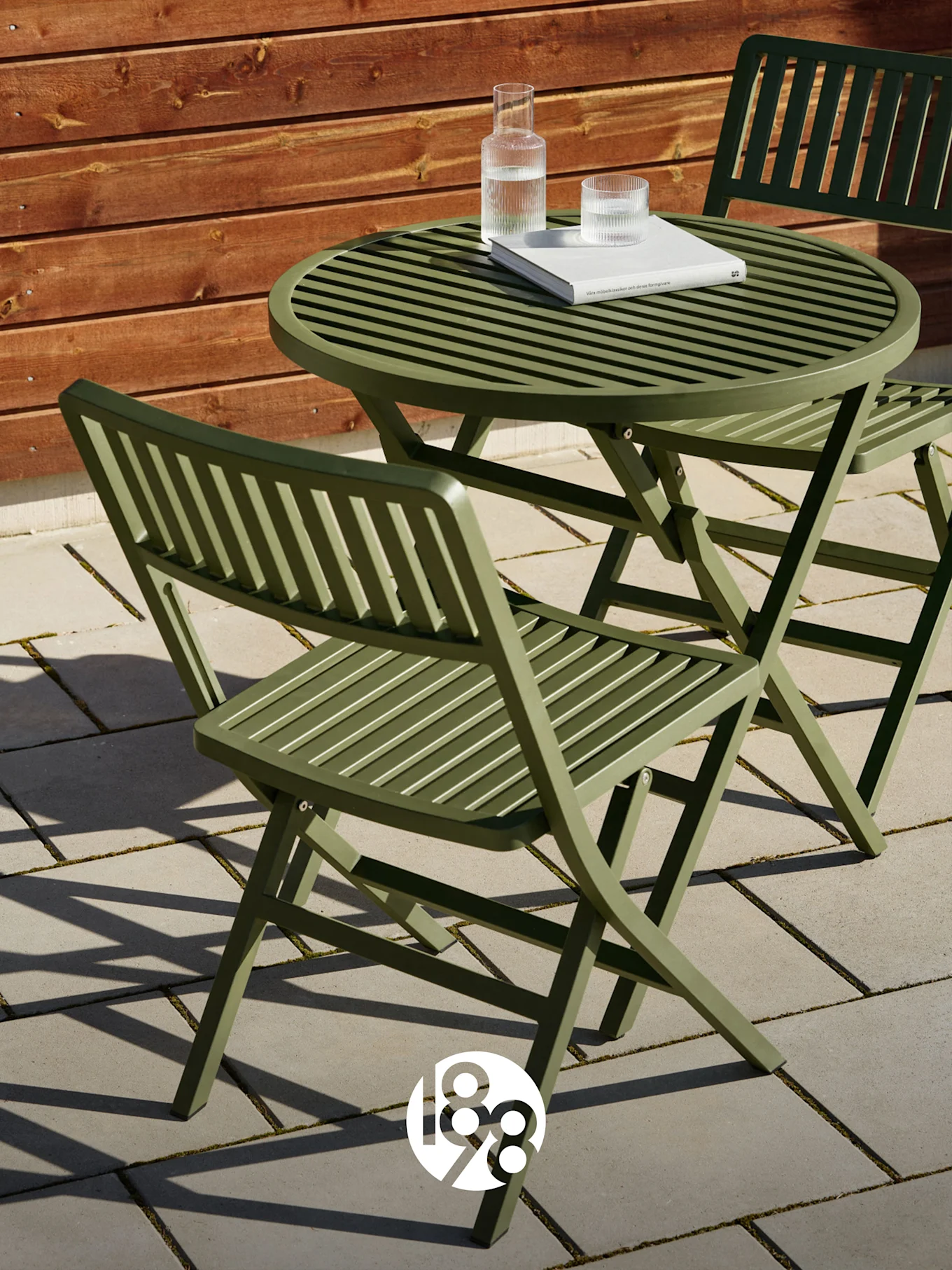 Kaksi vihreää ritilätaitettavaa tuolia ja yhteensopiva pöytä patiolla kirjan ja vesilasien kera.