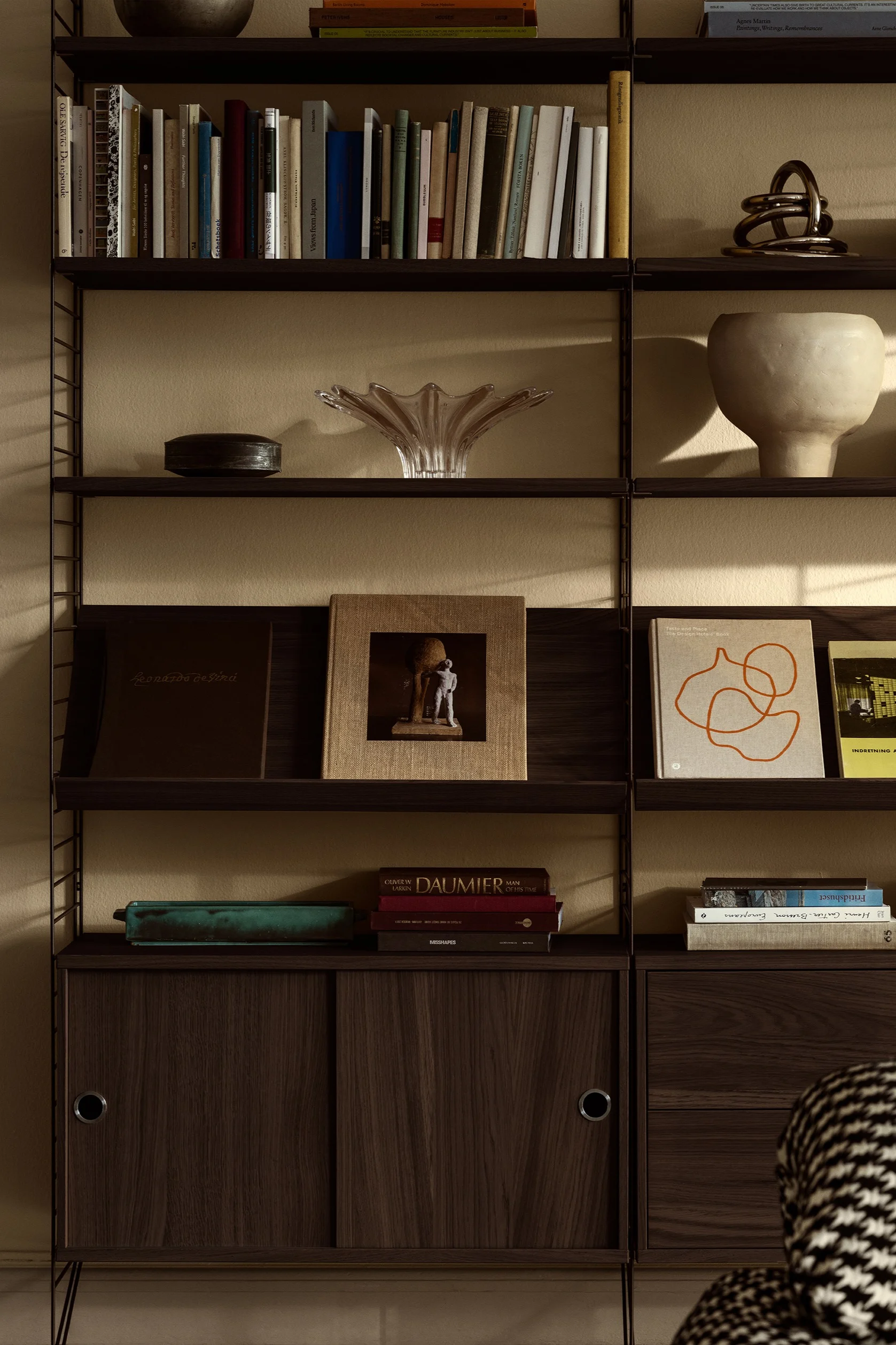 String-hyllyjärjestelmä sopii täydellisesti seinän koristeluun. Tässä näet hyllyjärjestelmän, jossa on henkilökohtaisia yksityiskohtia, kuten kirjoja ja kulhoja.