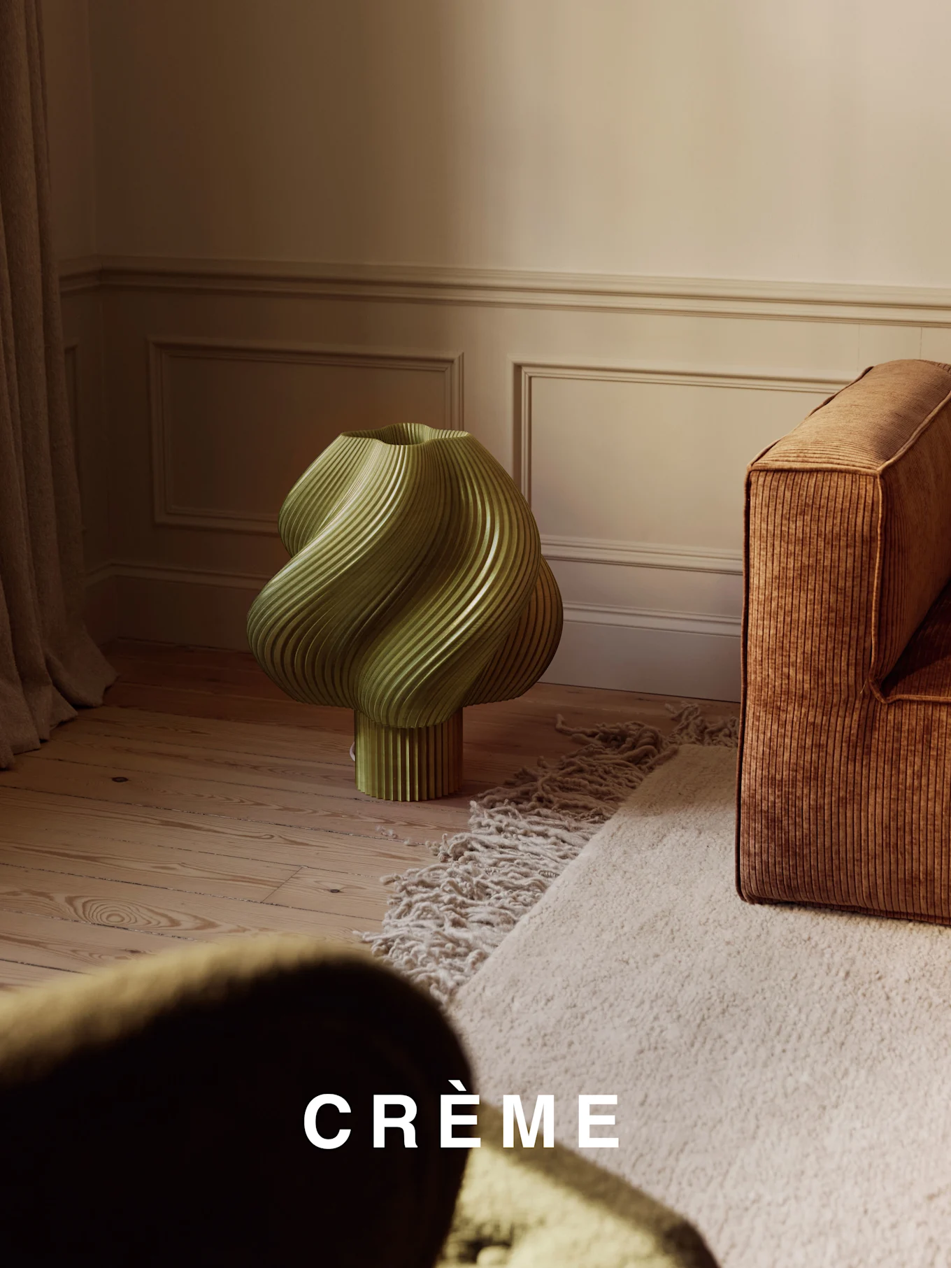 Vaaleanvihreä, kierretty uurrettu lamppu puulattialla, ruskean uurretun sohvan ja beigen nukkamaton vieressä.