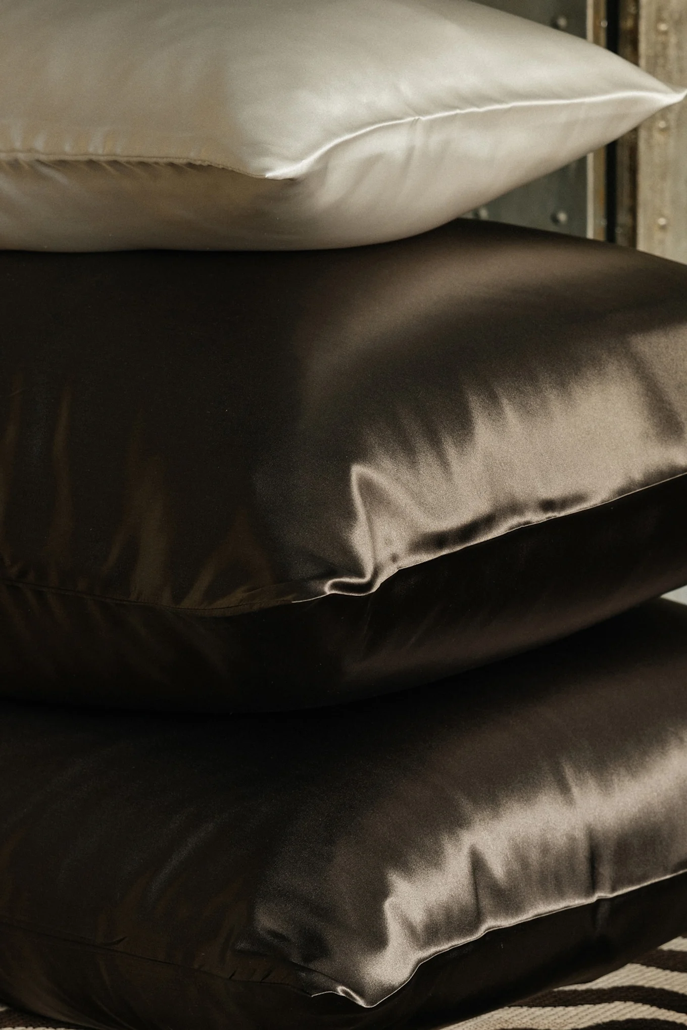 Pino kolmesta silkkityynystä, yksi vaalea ja kaksi tummanruskeaa.