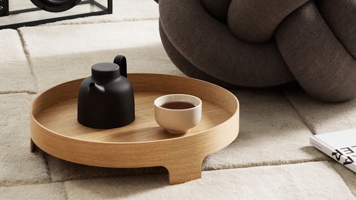 Lagom: Bridge-tarjotin seisoo matolla, jonka päällä on teekannu ja teekuppi, taustalla XL-tyyny, kaikki Design House Stockholmilta.