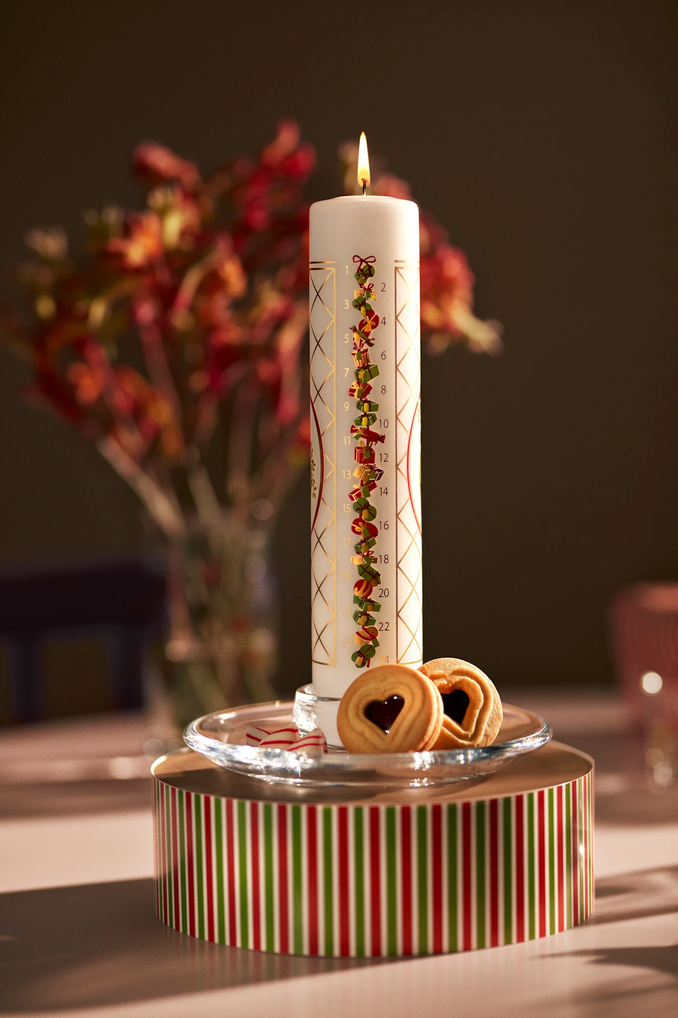 Holmegaardin adventtikynttilä seisoo juhlavalla laatikolla yhdessä keksien kanssa.