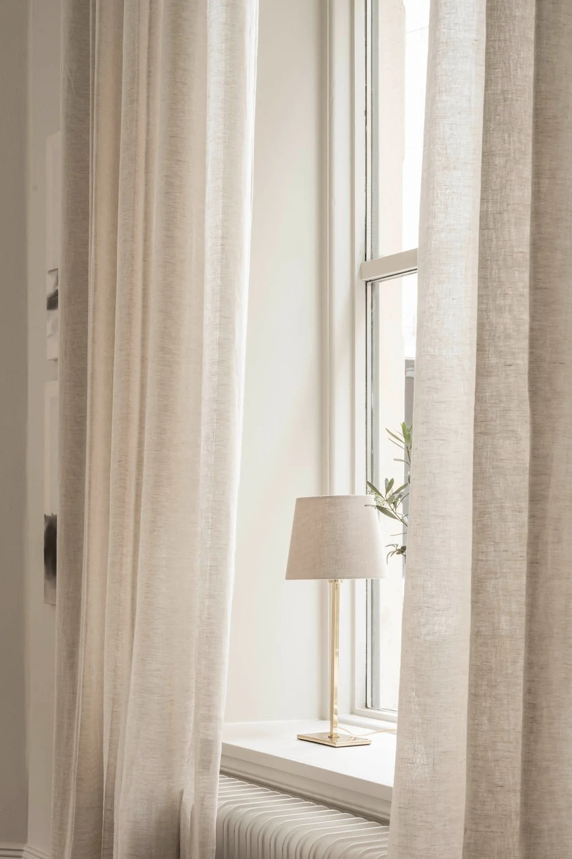 Watt & Veken pöytävalaisin seisoo ikkunalaudalla, ympäröimänä vaaleat verhot.