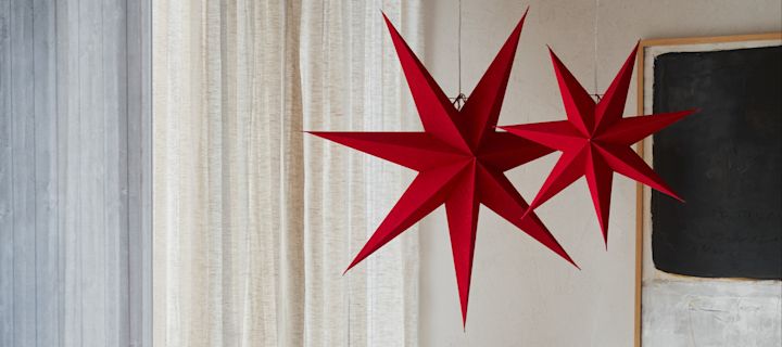 Kaksi Watt & Veken punaista paperista valmistettua tähtilyhtyä roikkuu olohuoneessa. 