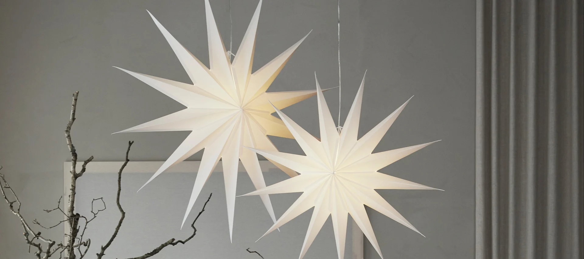 Kaksi Watt & Veken punaista paperista valmistettua tähtilyhtyä roikkuu olohuoneessa. 