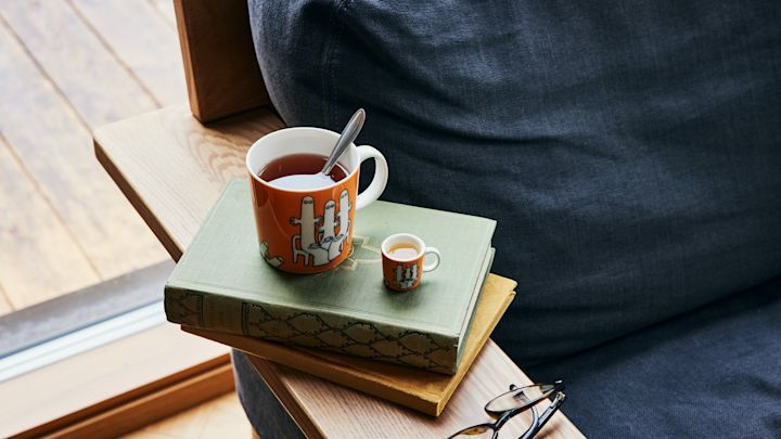 Oranssinvärinen Muumi-hahmo Hatifnatten teekuppi seisoo sohvan vieressä kirjojen päällä.
