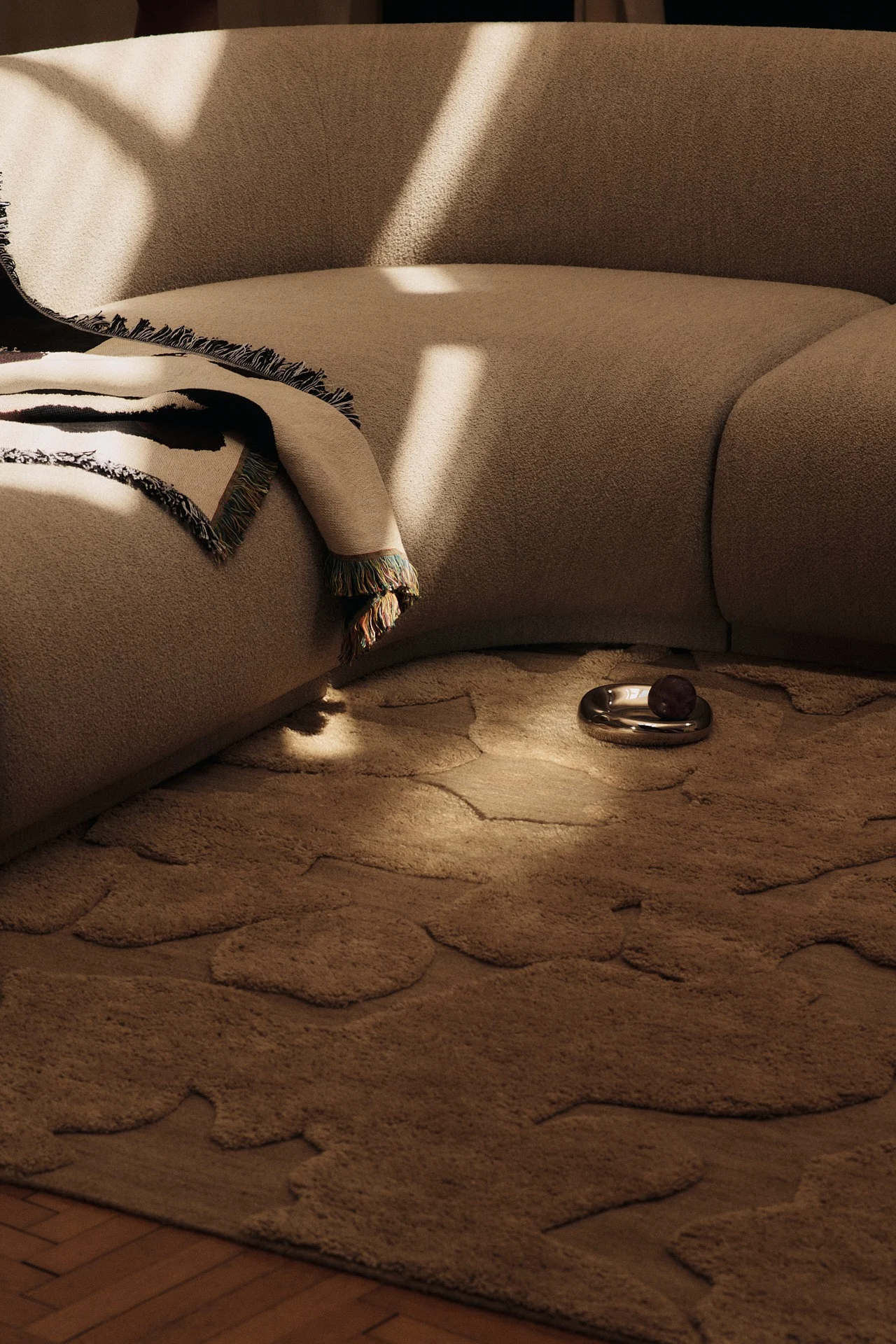 Vuoden 2026 värisuuntaukset heijastuvat tässä olohuoneessa, jossa vaaleanruskeat kalusteet on yhdistetty 1960-luvun inspiroimaan kombuchan sävyiseen kuviolliseen mattoon.