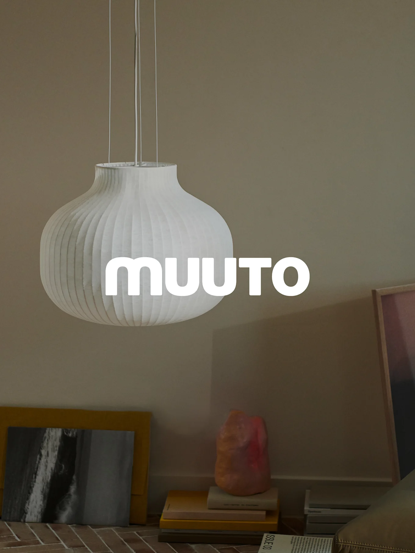 Valkoinen uurrettu kurpitsanmuotoinen riippuvalaisin 'MUUUTO'-logolla, beigessä huoneessa.