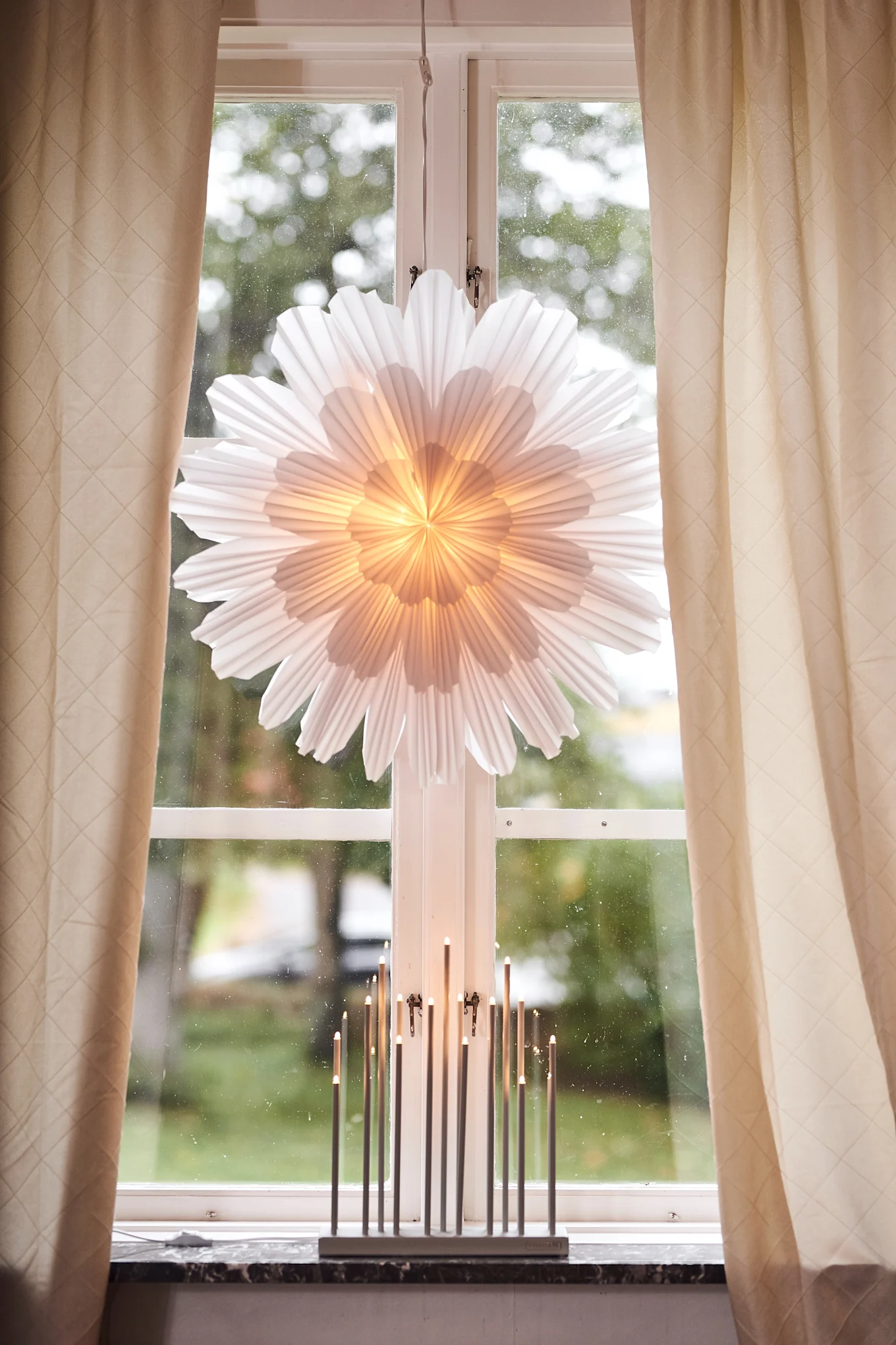 Juhli ensimmäistä adventtia koristelemalla kotisi adventtikoristeilla. Kuvassa näkyy Watt & Veken adventtitähti Snöblomma ripustettuna ikkunaan sekä ikkunalaudalla seisova kynttilänjalka Elflugan. 