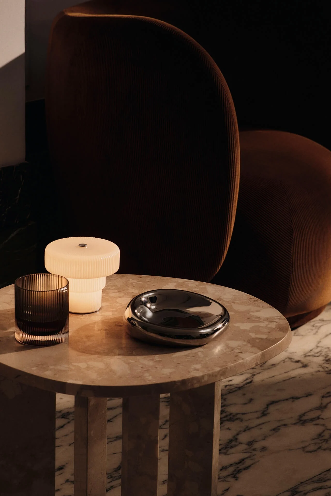 Ripple-kannettava lamppu seisoo kivisellä sivupöydällä Rico-nojatuolin vieressä.