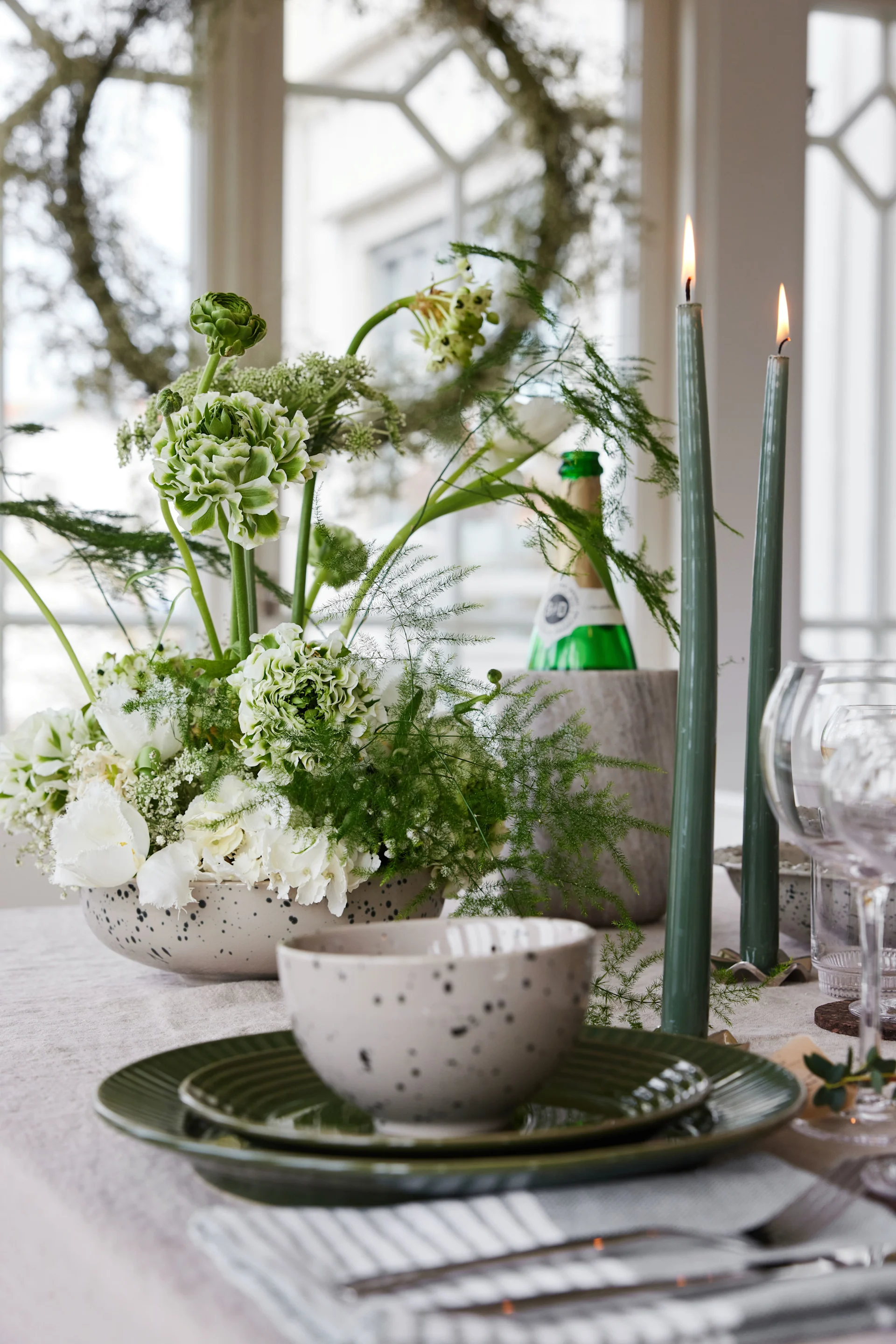 Katettu pöytä, jossa on lautasia, kukkia, kynttilöitä ja viinijäähdytin.