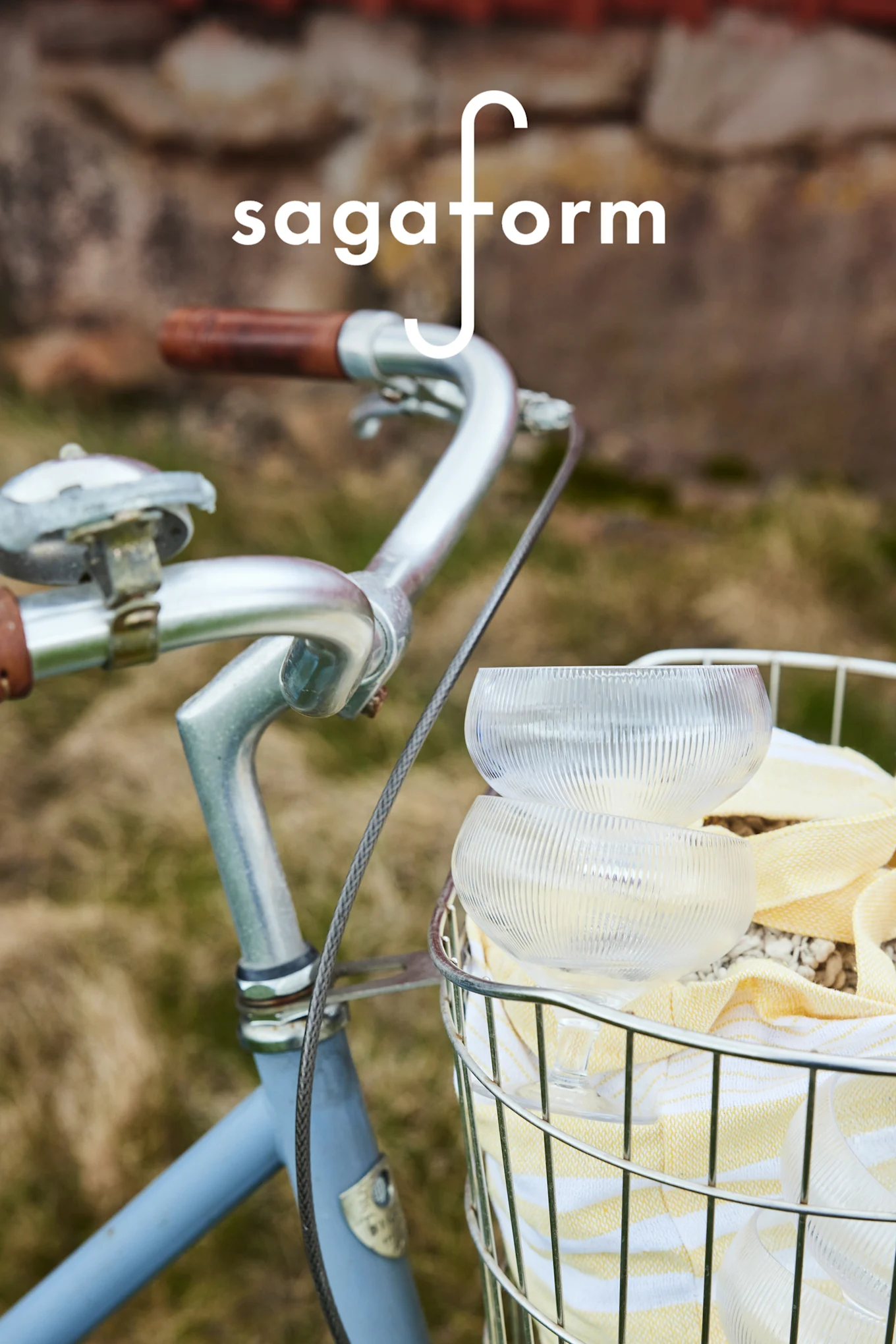 Kaksi kirkasta, uritettua lasikulhoa ja keltainen raidallinen pyyhe polkupyörän korissa. 'sagaform'-logo.