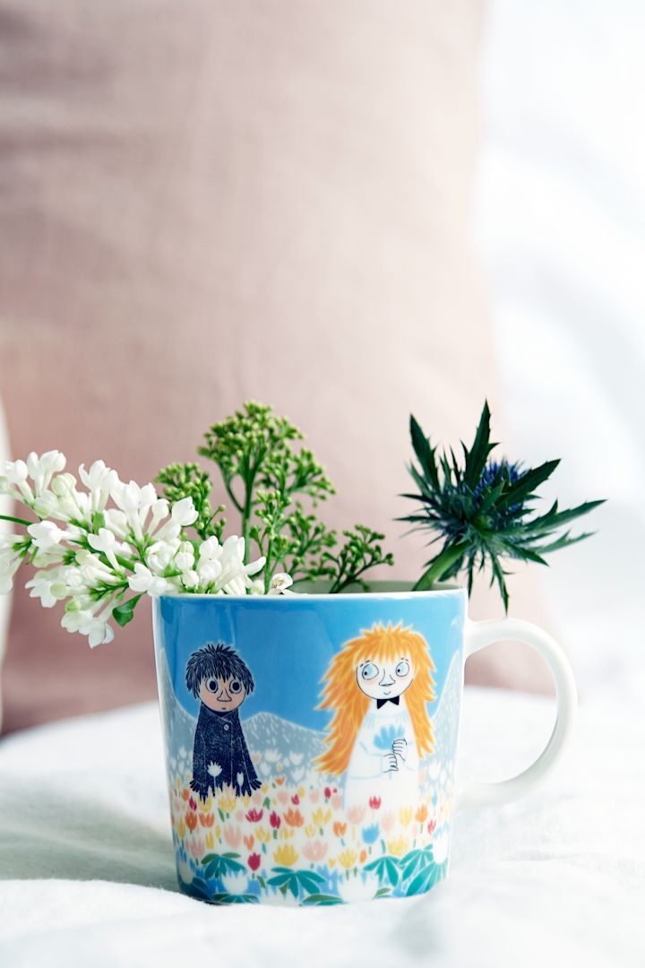 Muumikuppi ”Ystävyys” seisoo pöydällä, jonka sisällä on kukkia.
