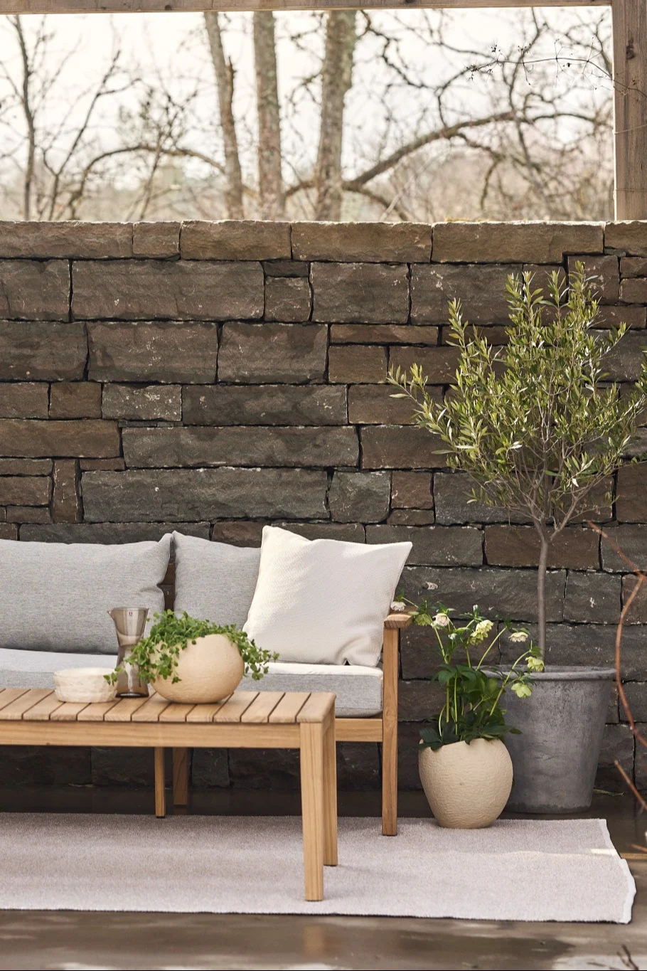 Viihtyisä terassi, jossa on matto, sohva ja sivupöytä sekä lukuisia kasveja.