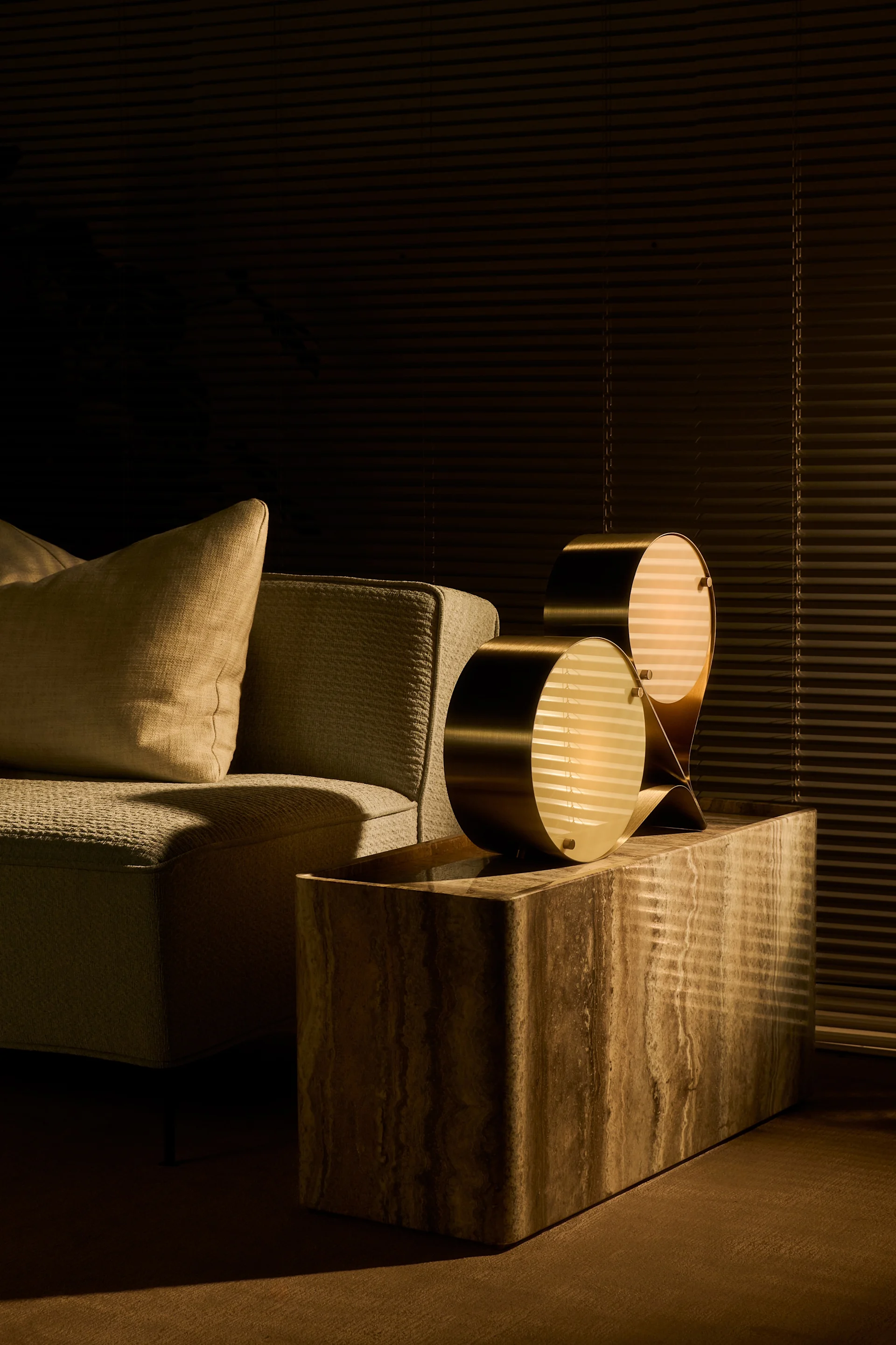 Luonnolliset värit ja kivi ovat syksyn 2025 sisustustrendejä. Tässä Coppia-lamppu seisoo Pietra-sivupöydällä, molemmat Gubin tuotteita, olohuoneessa.