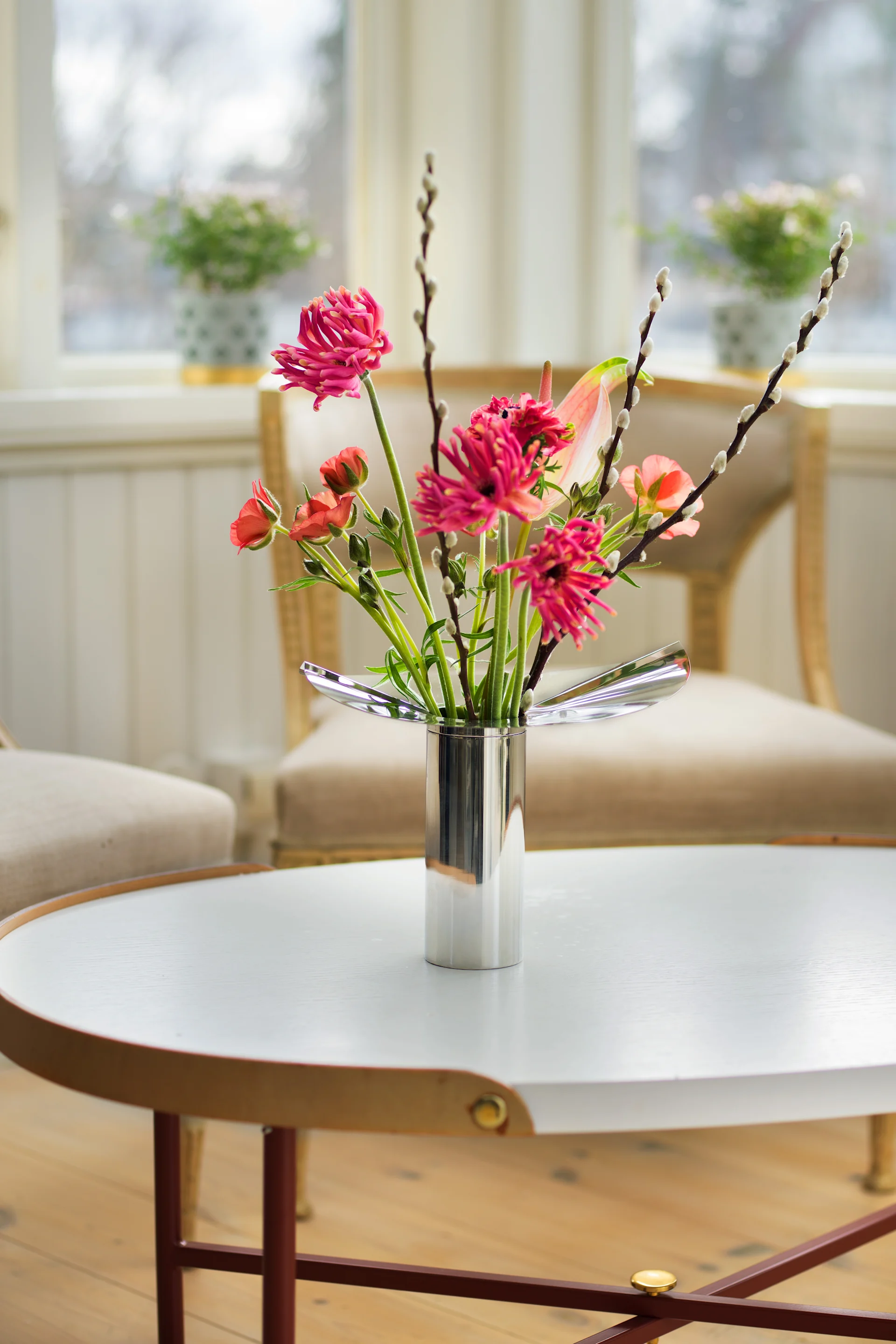 Pyöreä sohvapöytä on koristeltu Klongin kromivärisellä Löv-maljakolla/kynttilänjalalla, jossa on keväisiä kukkia.