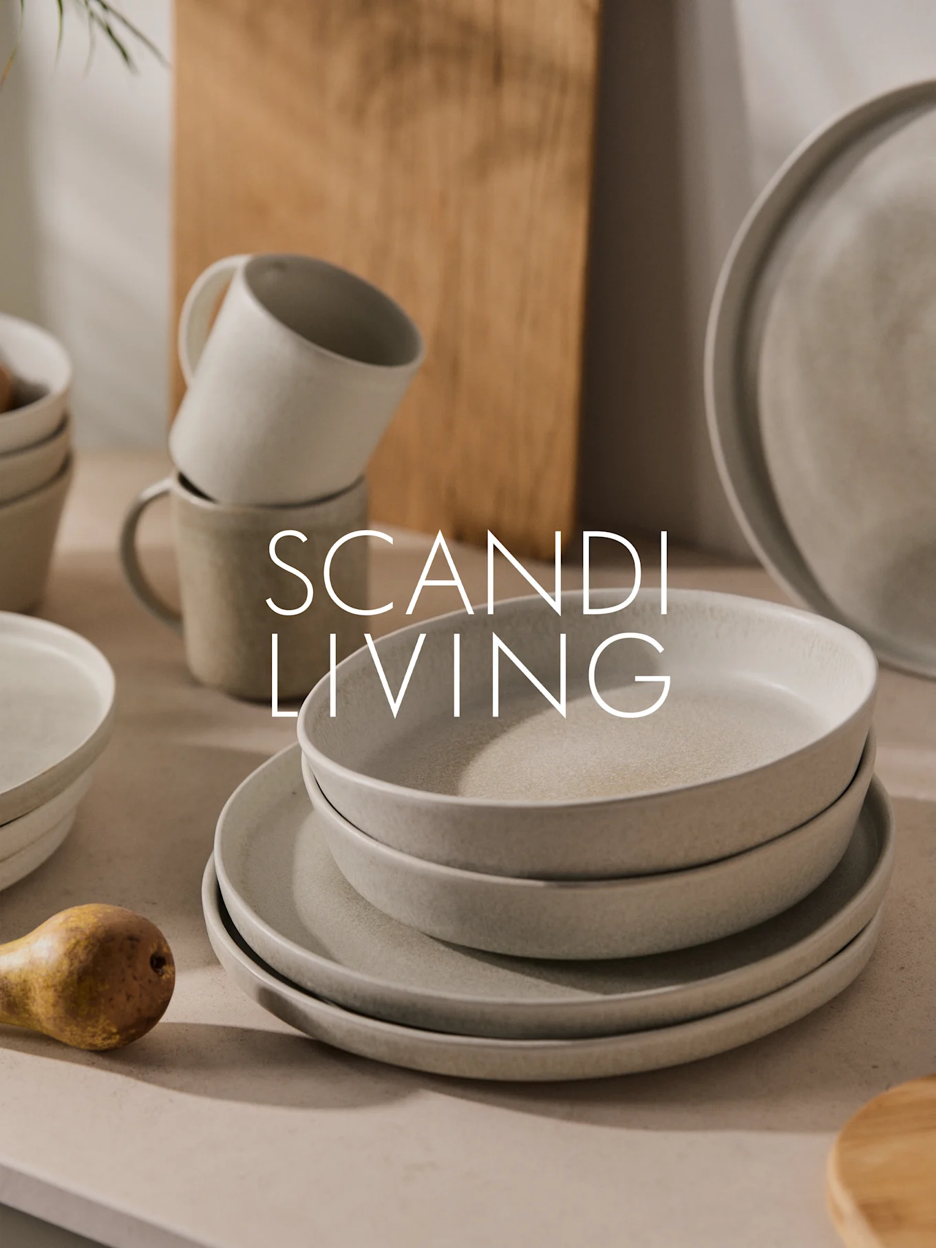 Pinoa vaaleita pilkullisia keraamisia lautasia, kulhoja ja mukeja, joissa on päärynä. Teksti: SCANDI LIVING.