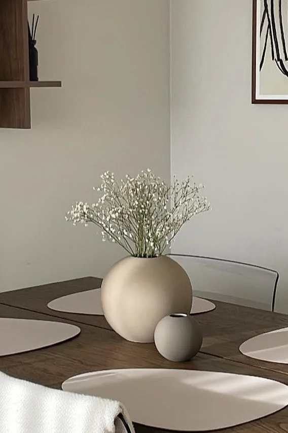 Hiekan ja harmaan värinen Ball-maljakko, jota on kahta eri kokoa, seisoo ruokapöydällä neutraalin värisessä ruokasalissa. 