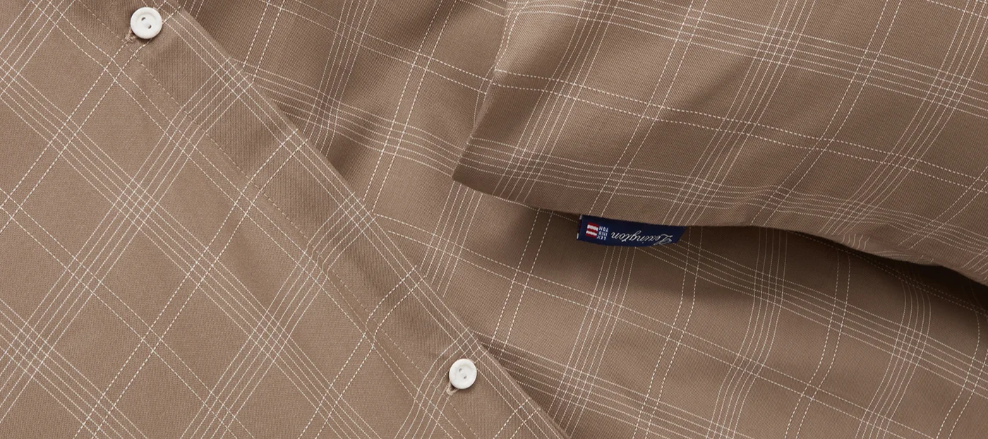 Lähikuva ruskeasta kankaasta, jossa on valkoinen ruutukuvio, kaksi valkoista nappia ja sininen Lexington-etiketti.