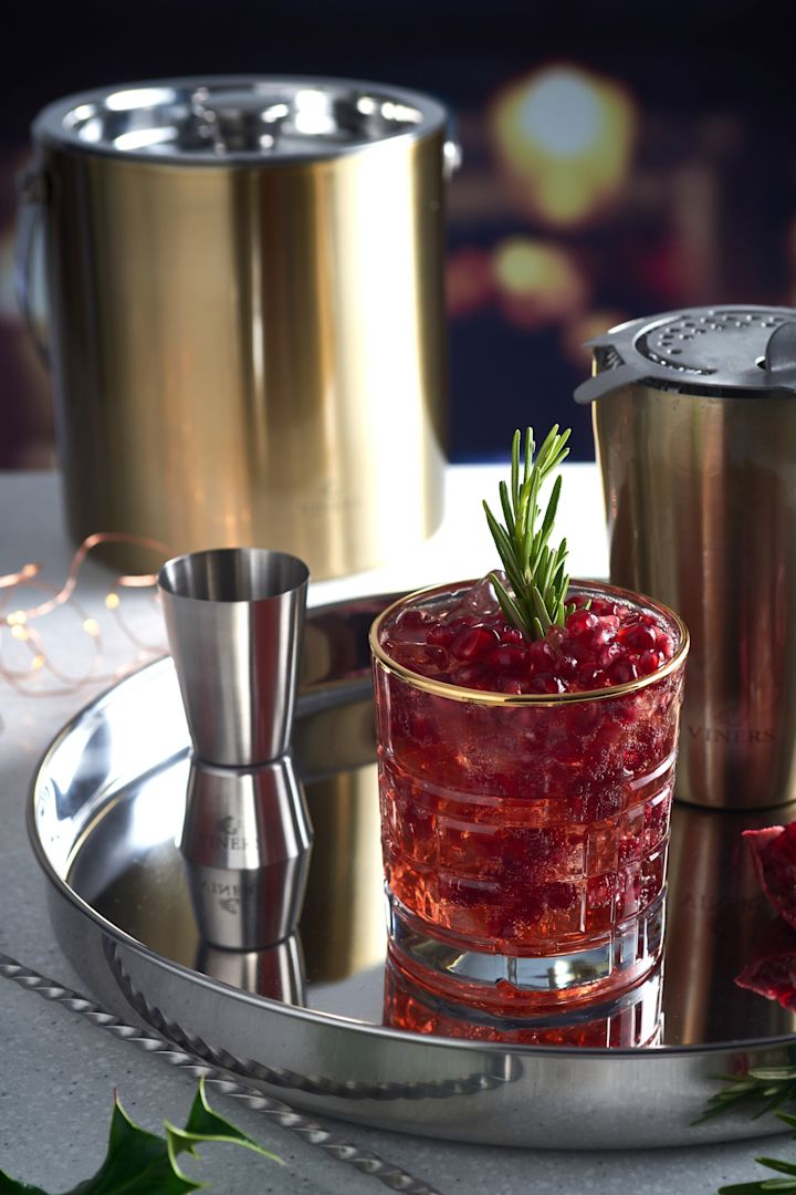 Mocktail on hopeatarjottimella, cocktail-tarvikkeiden, kuten shakerin ja Vinersin kultaisen jääpalakauhan vieressä.