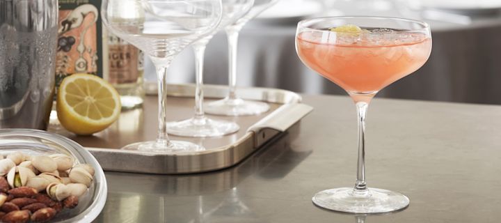 Holmegaard Cabernet -cocktaillasissa oleva greippimehulla valmistettu mocktail seisoo keittiön tiskillä, taustalla cocktail-tarvikkeet.