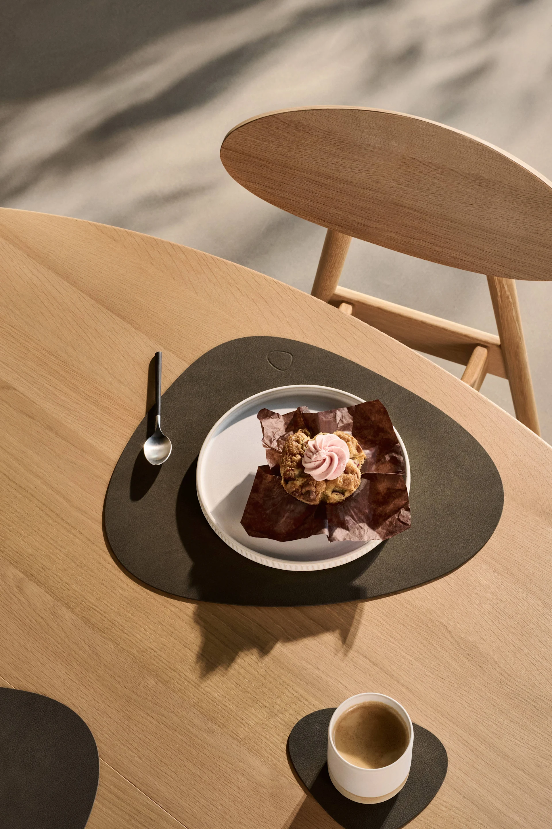Muffinssi vaaleanpunaisella kuorrutteella ja kahvi puupöydällä tummilla alustoilla.