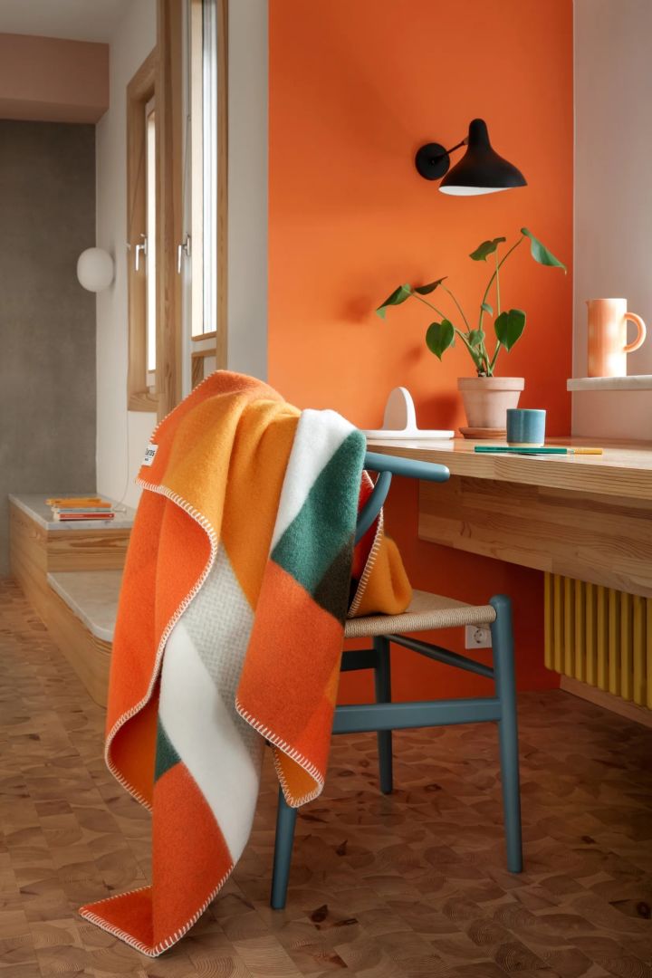 Oranssi on vahva väri sisustuksen väritrendeissä vuonna 2024. Tässä näet Røros Tweedin oranssin ja vihreän värisen Mikkel-peiton.