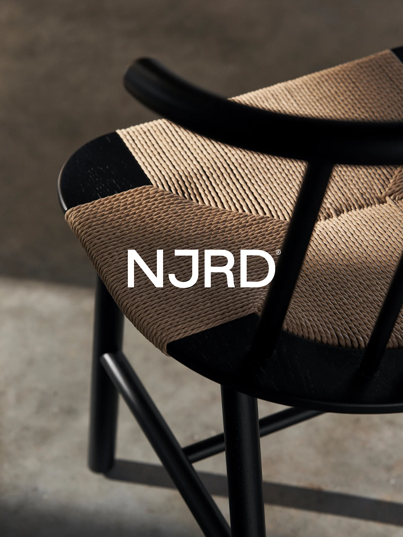 Lähikuva mustasta tuolista, jossa on kudottu vaaleanruskea istuin ja valkoinen 'NJRD'-logo.