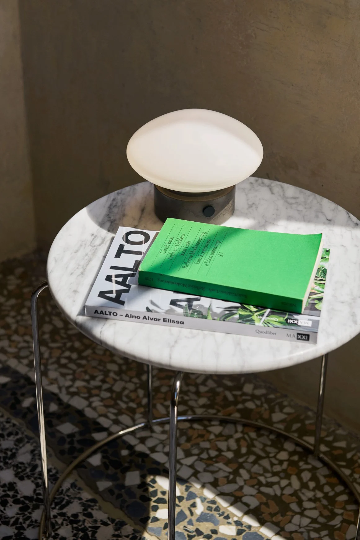 Mist AP12 -kannettava lamppu &traditionilta seisoo pienellä pyöreällä marmoripöydällä kirjojen kanssa. 
