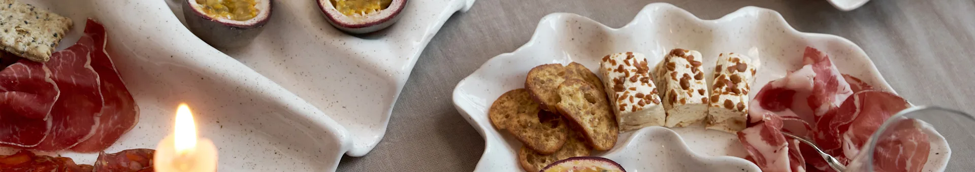 Alkuruokalautanen kahdella simpukankuoren muotoisella vadilla, jossa on leikkeleitä, keksejä, juustoa ja passionhedelmiä, sytytetty kynttilä.