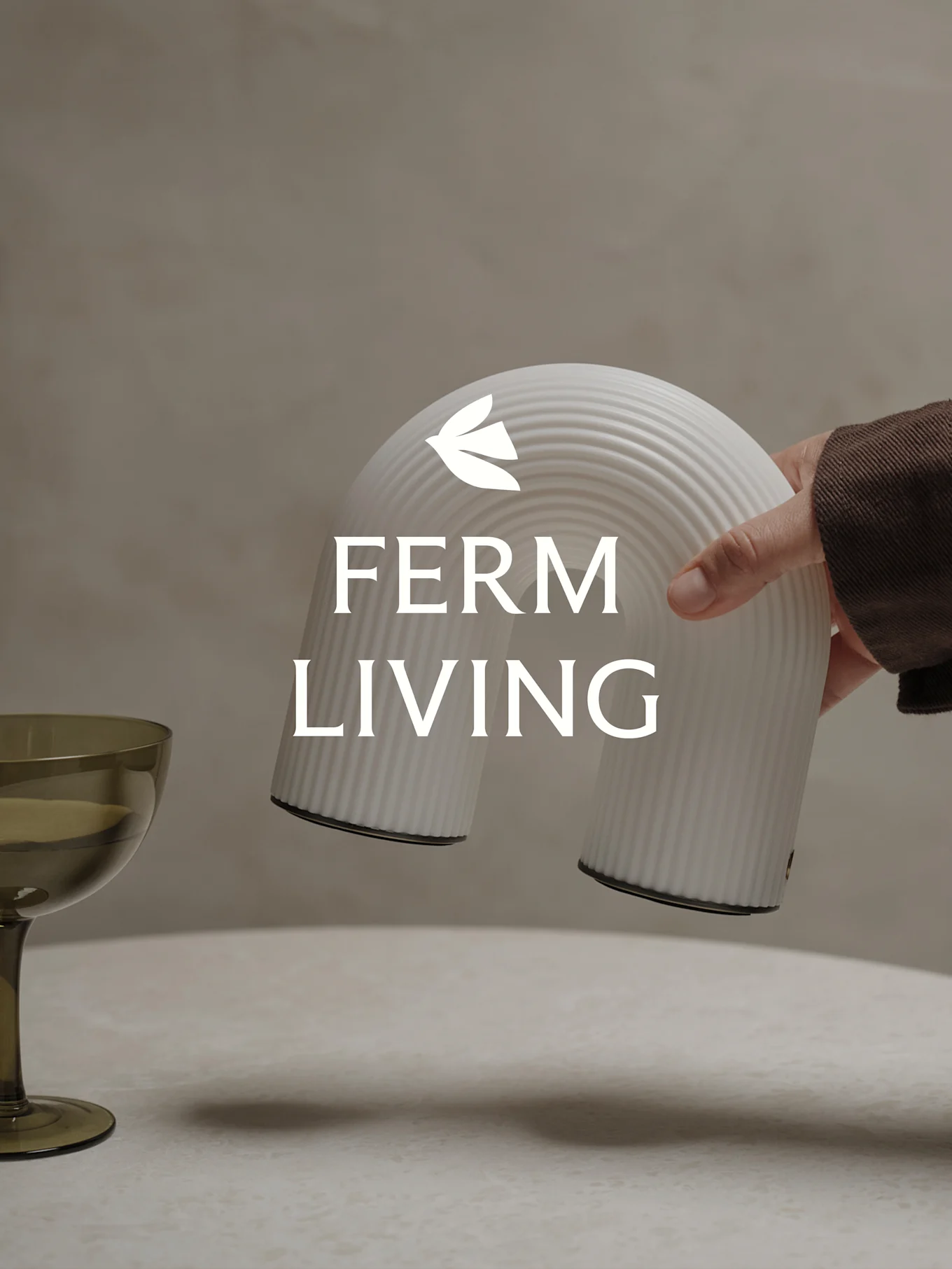 Käsi pitelee valkoista uritettua kaarenmuotoista koriste-esinettä, vihreän lasin ollessa lähellä.