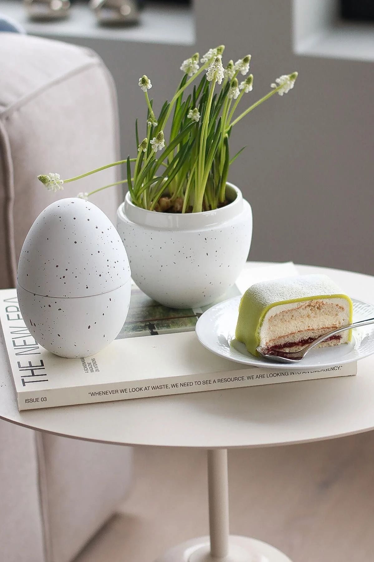 Sivupöydällä seisoo Cooee Designin valkoinen bonbonnière, jossa on kukkia, vieressä lautanen, jossa on Princesstarta, @picsbyellenin kotona.