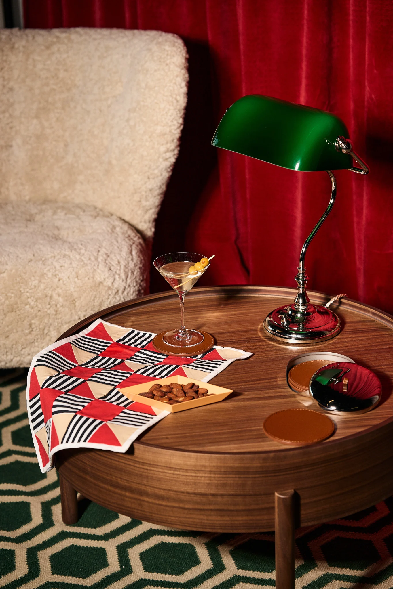 Martini, mantelit, vihreä pankkiirivalaisin puupöydällä, geometrinen kangas, kermanvärinen nojatuoli, punaiset verhot.
