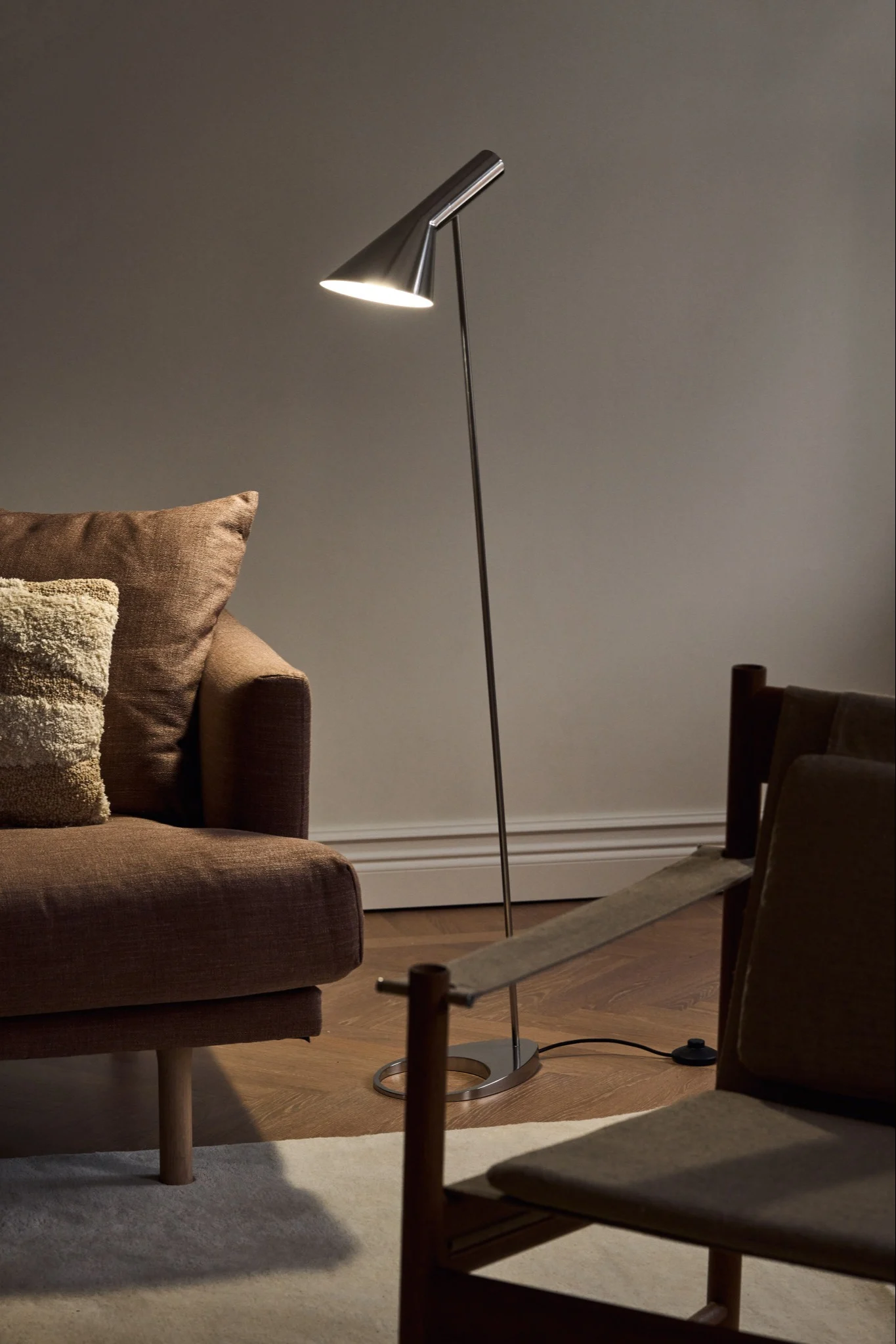 Skandinaaviset lamput: Louis Poulsenin kromivärinen AJ-lattiavalaisin seisoo yksinkertaisessa olohuoneessa sohvan vieressä.