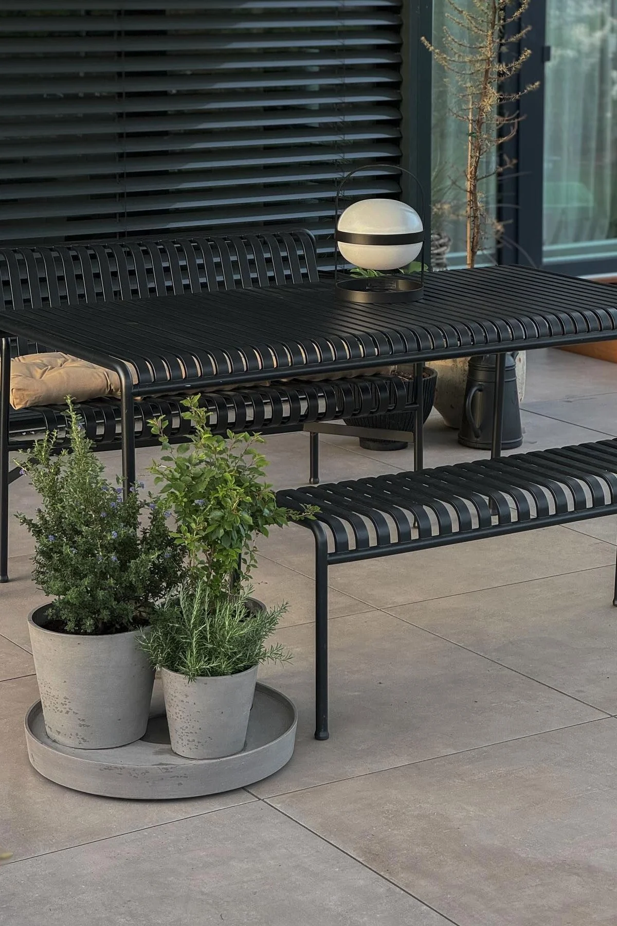 Palissade-malliston puutarhakalusteet ovat @grauschwarzlieben terassilla. Edessä on kukkaruukkuja, joissa kasvaa yrttejä, ja pöydällä on Rosendahlin Soft Spot -aurinkokennovalaisin.