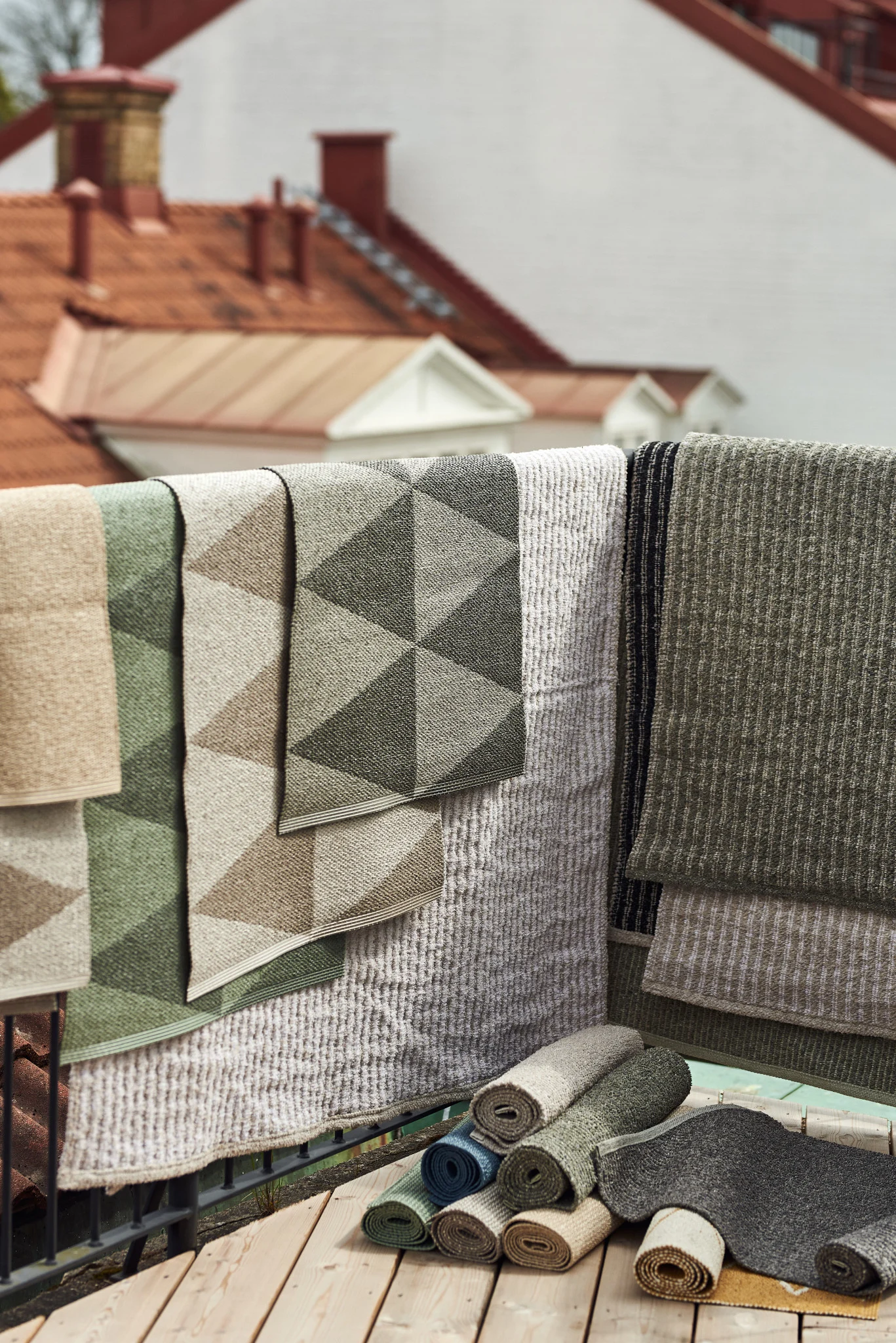 Ulkomatto: Tässä näet Scandi Livingin lukuisia erikokoisia, -materiaalisia ja -värisiä ulkolattiamattoja roikkumassa parvekekaiteen päällä.