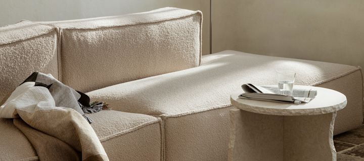 Beige olohuone sohvan kanssa, sivupöytä ja viihtyisä viltti merkiltä Ferm Living.