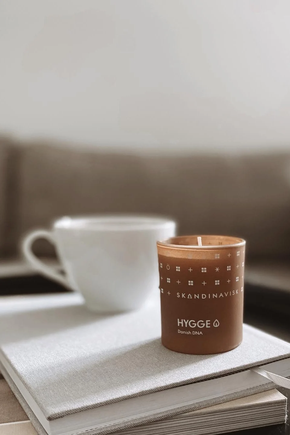 Skandinaviskin Hygge-kynttilän kaltainen tuoksukynttilä, joka on tässä kuvassa pinottu kirjojen päälle sohvapöydälle, on loistava valentinepäivälahja kodikkaita iltoja varten.