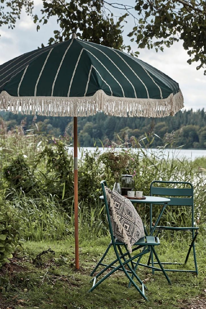 Boho-koristeet puutarhaan: House Doctorin vihreä, hapsullinen aurinkovarjo puutarhassa, vieressä pieni istuinryhmä.