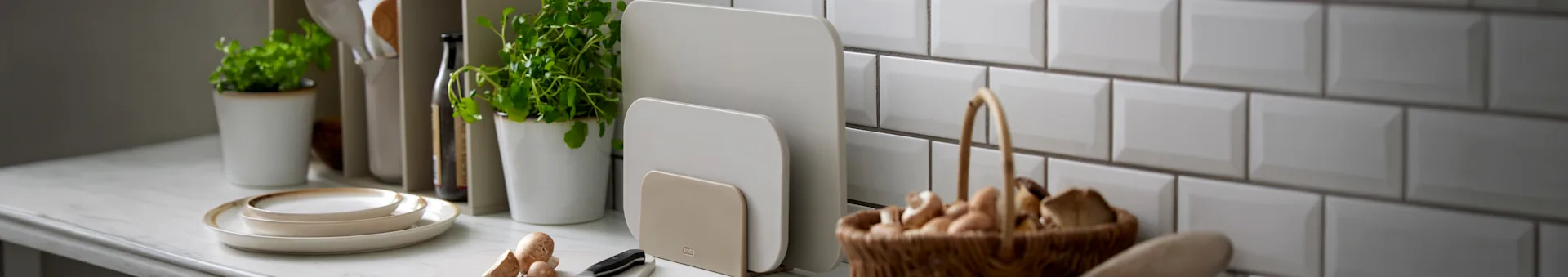 Kaksi beigeä leikkuulautaa telineessä keittiön työtasolla muiden ruoanlaittotarvikkeiden kanssa.