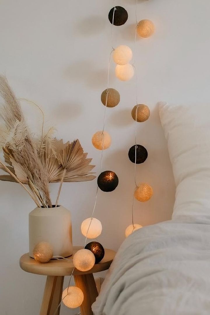 Beigen ja ruskean sävyillä varustettu Irislightsin Biscotti-valosarja, joka on ripustettu tässä sängyn viereen, on täydellinen boho-tyylinen koriste.